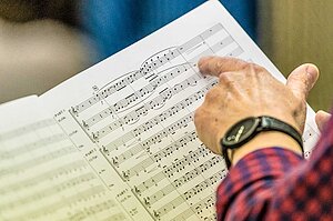 Hand einer Dirigentin zeigt auf eine Stelle im Notenblatt